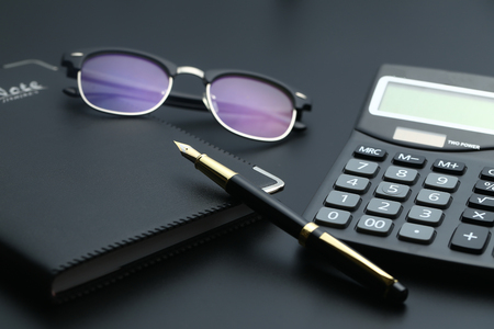 golden pen,notebook,calculator and glasses on black deskの写真素材