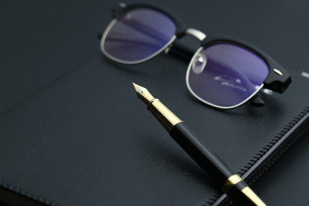 golden pen,notebook,calculator and glasses on black deskの写真素材