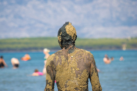 Unrecognizable person in healthy mud on beach back portret viewの写真素材