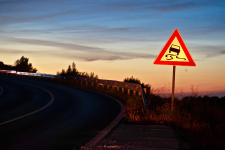 Curvy road sliding danger traffic sign at sunset next to road laneの写真素材