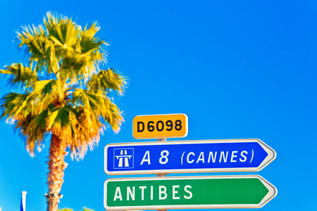 Cote d Azur road sign to Antibes and Cannes, palm and blue sky background, French rivieraの写真素材
