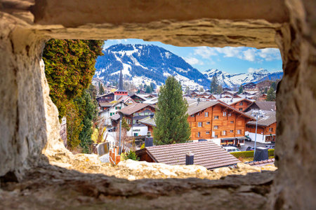 Idyllic Alpine village of Gstaad view through stone window, luxury winter destination in Switzerland