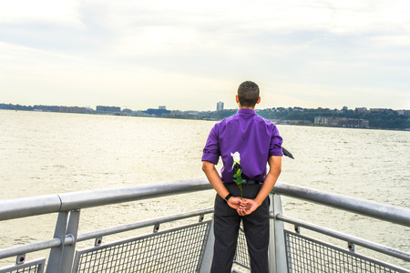 Dressing in a purple shirt and gray pants, a black tie flowing in the wind, a young guy is standing...