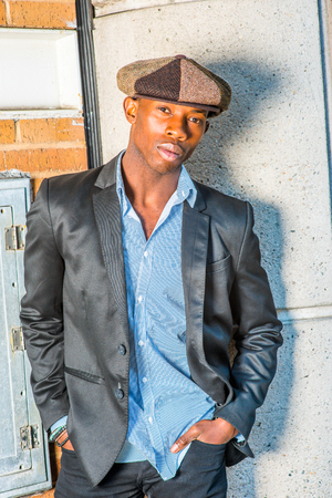 Portrait of Young Black Guy.  Wearing fashionable Newsboy cap, black blazer, unbuttoned,  a young black guy is standing on the corner of the street, looking at you. Man Urban Fashion.の写真素材