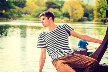 Man Waiting for You. Wearing a striped T shirt, brown corduroy pants, a young handsome guy is sitting by a lake, inclining half body, looking faraway, greeting You.の写真素材