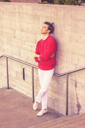 Young blonde professional, wearing red sweater, white pant, casual fashion shoes, crossing arms, leaning back against wall, sad, thinking, lost in thought, Retro filtered look.の写真素材