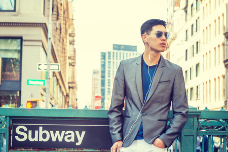 Young Asian American Man traveling in New York, dressing in gray blazer, white pants, wearing...