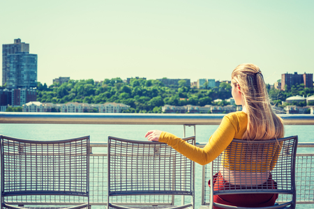 Empty Chairs for You. lonely girl waiting friendship. Wearing yellow long sleeve fit crop T shirt, young woman with long blonde hair sitting on chair by Hudson River in New York, facing New Jersey.の写真素材