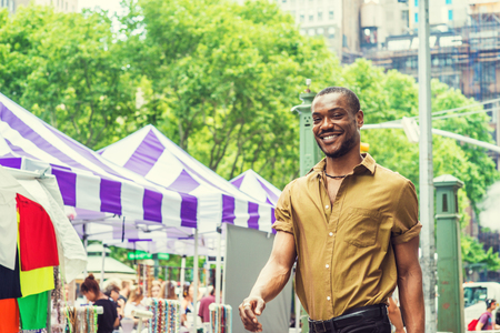 Summer Street Fair and Flea Market in New York. Young African American Man shopping, traveling in New York, wearing green short sleeve shirt, walking by street in Midtown of Manhattan, smiling.の写真素材