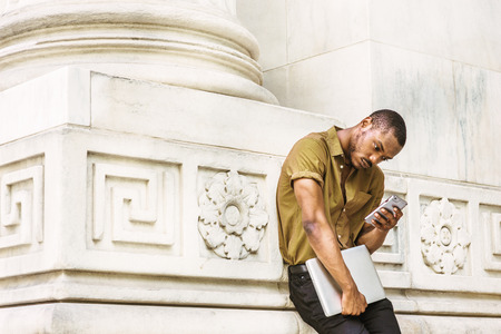 Young African American Businessman working in New York, wearing green short sleeve shirt, carrying...