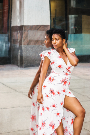 Young African American Woman with short afro hairstyle, wearing patterned dress, standing against mirror in New York, looking down, sad, thinking. Concept of self assured, self esteem, self checking.
の写真素材