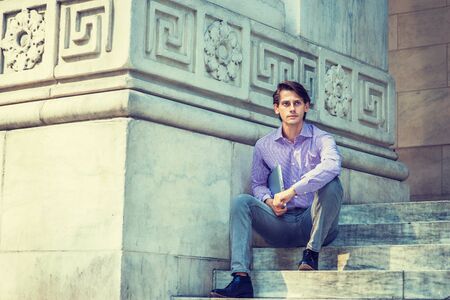 Young Businessman wearing patterned shirt, black jeans, leather shoes, carrying laptop computer, sitting on stairs of vintage office building, looking up, thinking, lost in thought. Filtered effect.の写真素材
