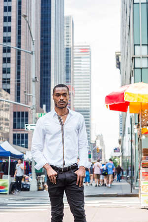 Young African American Man with beard, wearing white long sleeve shirt, black pants, standing on...
