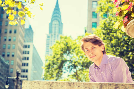 Young Handsome Man relaxing outside in Manhattan, New York in beautiful sunny day. Tall buildings, trees on background.の写真素材