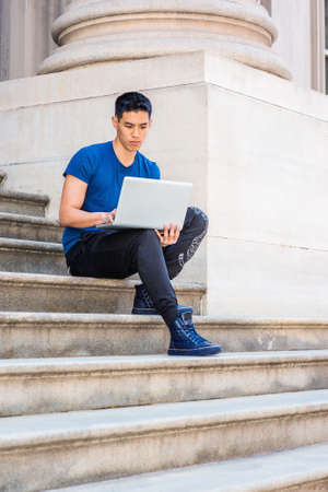 Young Asian American College Student studying in New York City, wearing blue T shirt, black pants,...