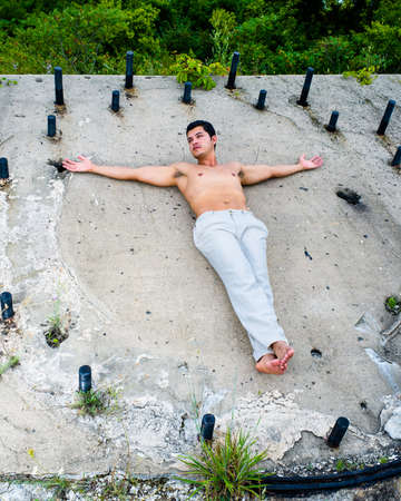A masculine guy, wearing a white pants, barefoot and half naked, is climbing a slope with the help of metal rodsの写真素材