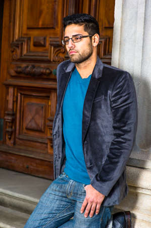 Dressing in a dark purple woolen blazer, sweater and jeans, wearing glasses, a young scholar with...