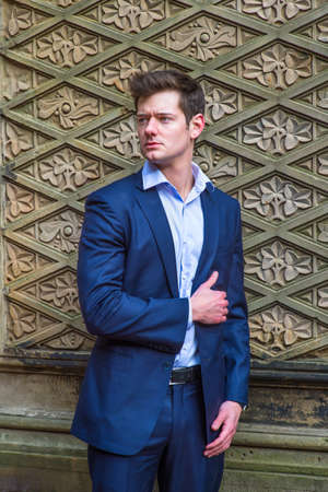 Dressing in a blue slim fit suit and a light blue under shirt, a young handsome businessman is confidently standing there with his hand on heart.の写真素材