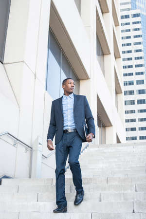 A young handsome black businessman is walking down on steps from a business building.の写真素材