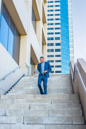 Holding a tablet computer, a young handsome black businessman is reading while walking down stairs...