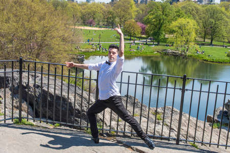 Stretching arms and legs, a young handsome guy is dancing in a park.
