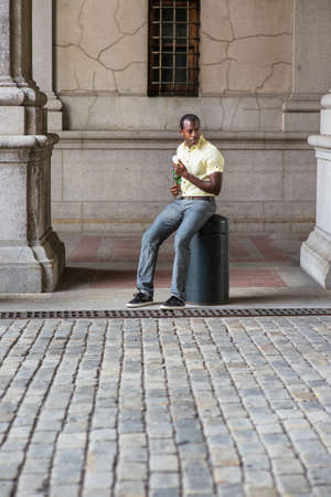 Dressing in a light yellow shirt, gray pants and black shoes, a young attractive black guy is...