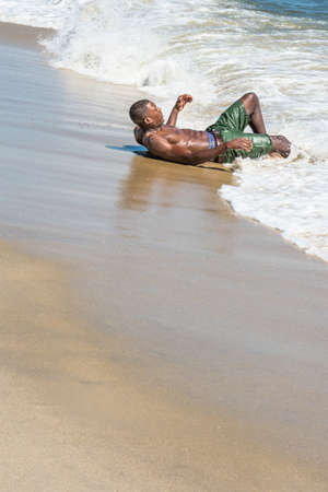 A well built young  black guy, half naked,  is  lying on the beach and playing with waves of water.の写真素材