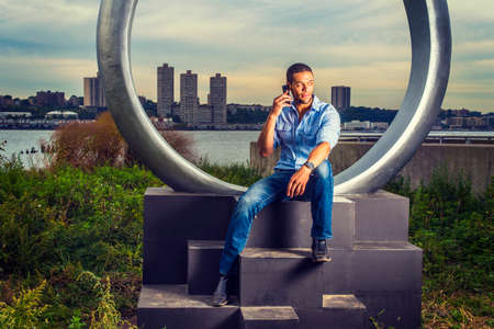 Modern Life. Wearing a light blue shirt, blue jeans, a young handsome college student with a little...