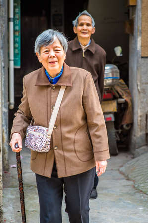 Senior Man and Woman Walking Outside. A  senior couple, 80 years old, smiling, is going outside, welcoming you, woman holding a walking stick.の写真素材