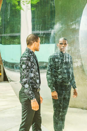 Man looking at mirror. Tough African American businessman, walking by metal mirror wall, looking at...