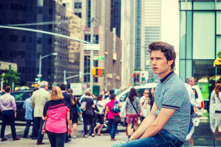 European student in New York. Wearing blue pattered short sleeve shirt, jeans, young guy sitting on...