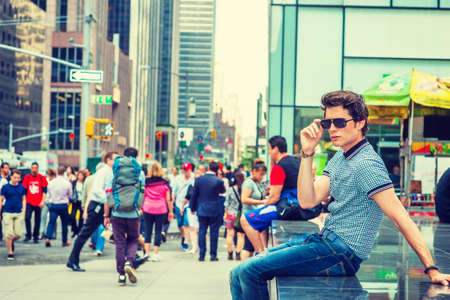 European college student traveling in New York. Wearing blue pattered short sleeve shirt, holding...