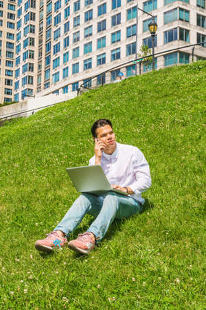Way to Success. Wearing white shirt, jeans, sneakers,  a college student sitting on green hill in...