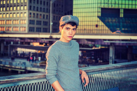 Portrait of New York City Boy. Wearing newsboy cap, knitting sweater, Asian American college student standing in business district with high buildings, looking at you.の写真素材