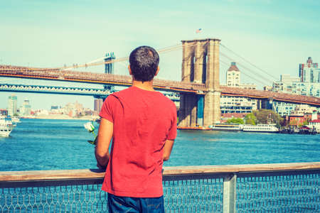 I missing you, waiting for you. East Indian American man wearing red T shirt, standing by river,...