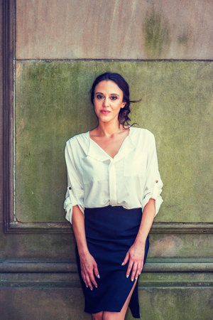 Beautiful lady, wearing white shirt, black skirt, standing against vintage wall outside, relaxing, taking break.の写真素材