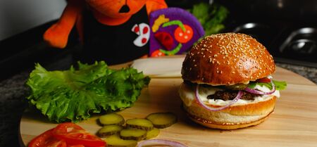 Juicy burger, sliced cucumbers, salaa leaves and tomatoes lie on a wooden tray Beautiful concept backgroundの写真素材