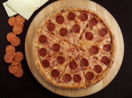 Large pepperoni pizza with ingredients on a black top view background top view photoの写真素材