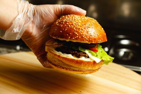 Man's hand in gloves holds juicy burger against dark closeup background Beautiful concept backgroundの写真素材