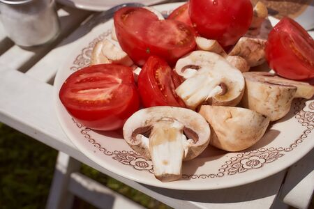 Vegetables for grilling tomatoes and mushrooms on a white plateの写真素材