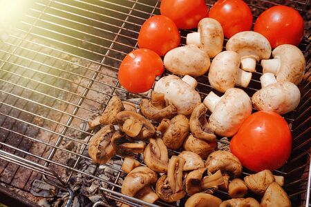 vegetables for grilling tomatoes and mushrooms mushrooms lie on the grill, which stands on a grill with coals Closeup effectの写真素材