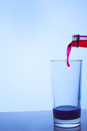 pour red wine into a glass cup with blue liquid. Hight quality photoの写真素材