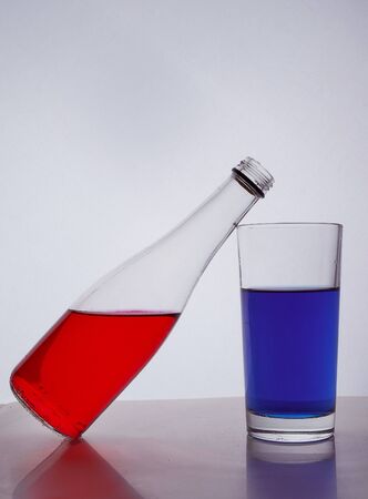 composition from a bottle and glasses with multicolored liquid on a white background. The bottle rests on a glass. Hight quality photoの写真素材