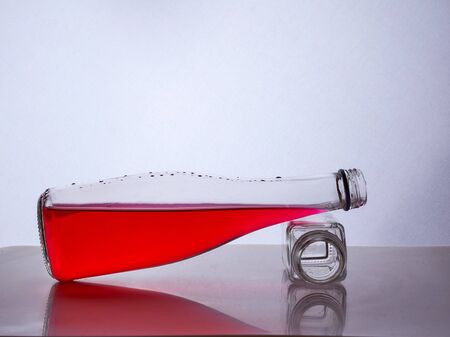 glass bottle with red liquid inside lies on a small bottle of white background. Hight quality photoの写真素材