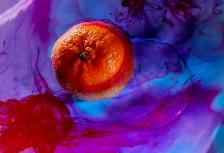 ripe tangerine floating in colored liquid closeup . High quality photoの写真素材