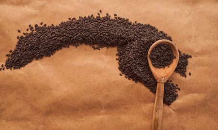 Black sesame seeds are scattered over a brown background with a wooden spoon. High quality photo