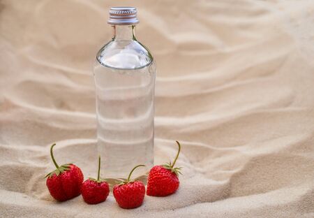 bottle water and ripe red strawberry berries lie on the sand. High quality photoの写真素材