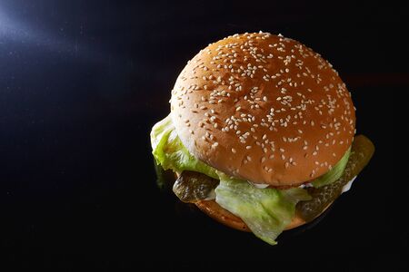 Juicy burger with onion rings, cucumbers, lettuce, cheese on a black background. With copy space. High quality photoの写真素材