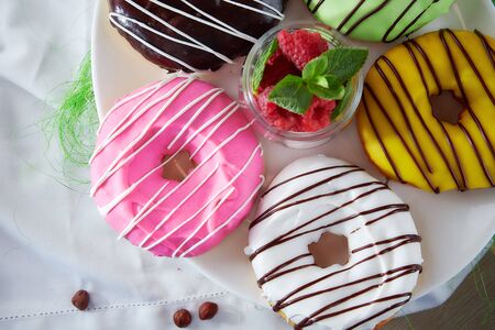 Doughnuts with multi-colored glud on white tablecloths and raspberries . High quality photoの写真素材