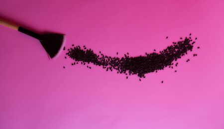 cosmetic brush sweeps black sesame seeds from a pink background. High quality photoの写真素材